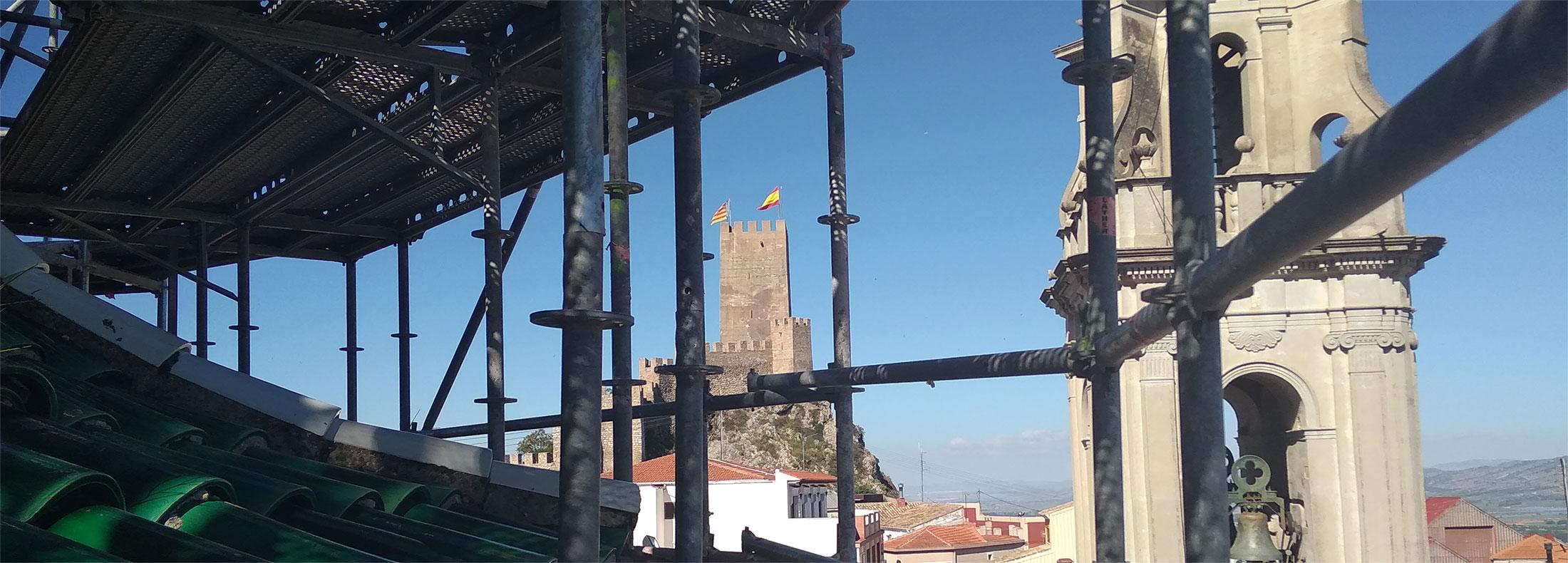 Vista de campanario en primer plano y castillo al fondo desde el interior de un andamio