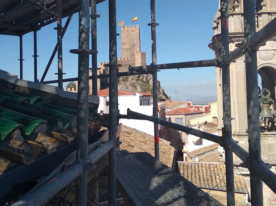 Vista de campanario en primer plano y castillo al fondo desde el interior de un andamio
