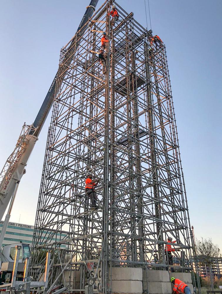 Vista desde abajo de andamio con grúa móvil y varios trabajadores subidos a la estructura.