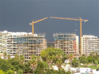Un parque con dos edificios en construcción al fondo, con instalación de andamios en la parte superior y dos gruas.