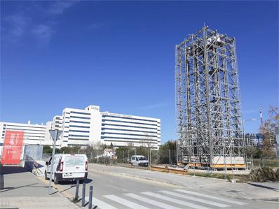 Calzada con aceras y un andamio en la parte derecha. Al fondo el edificio de un hospital.